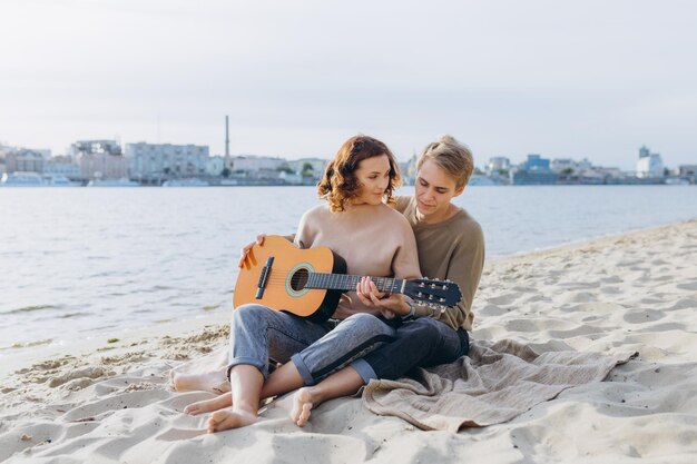 Rapariga aprendendo guitarra com professor do sexo masculino ao ar livre na praia mostrando acordes de guitarra