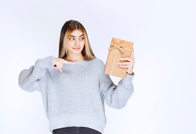 Rapariga com camisola cinzenta, segurando uma caixa de presente de papelão.