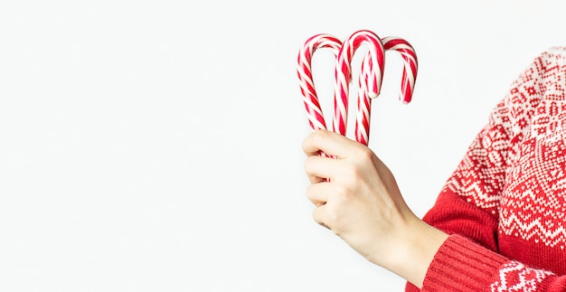 Rapariga com uma camisola de natal detém bastões de doces de natal em um fundo branco, close-up. fundo de natal. bandeira. copie o espaço.