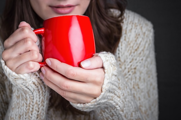 Rapariga com uma camisola leve a segurar numa chávena de café vermelha