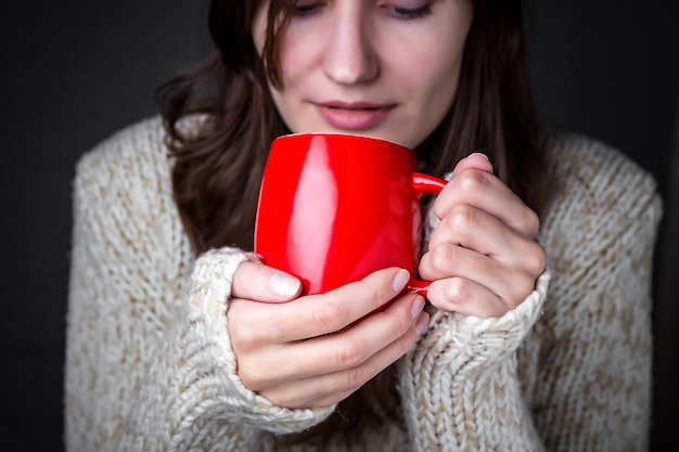 Rapariga com uma camisola leve a segurar numa chávena de café vermelha