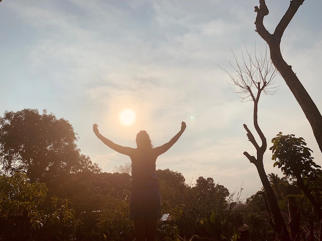 Foto rapariga de silhueta com os braços levantados de pé contra o céu durante o pôr do sol