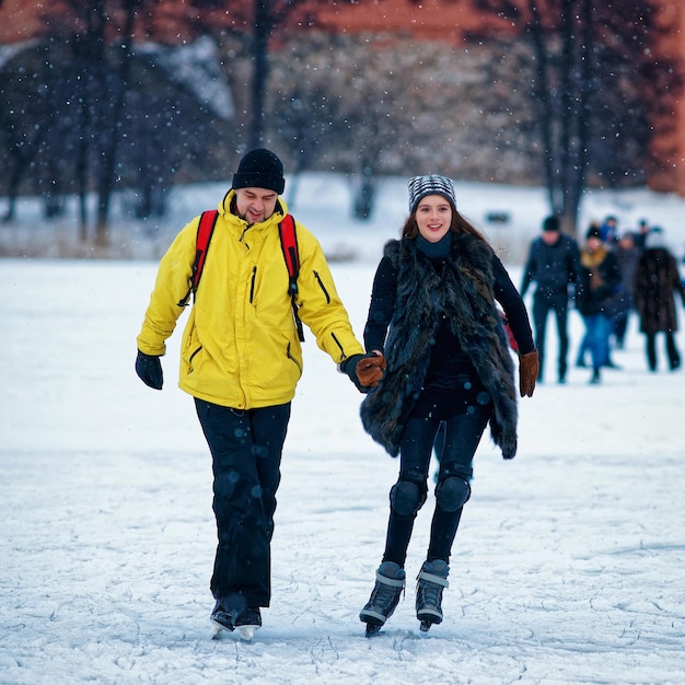 Rapariga e homem patinando no gelo no rinque de inverno coberto de neve em trakai, na lituânia. foco seletivo em movimento