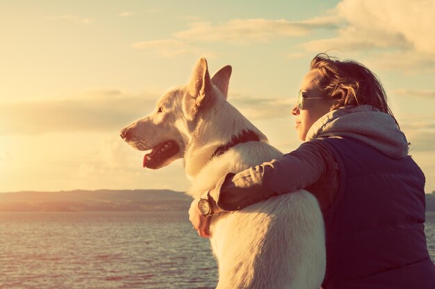 Foto rapariga hipster brincando com cão em uma praia durante o pôr do sol forte efeito de flare da lente