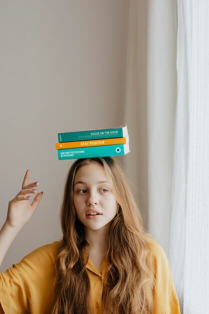 Rapariga loira alegre a equilibrar livros na cabeça