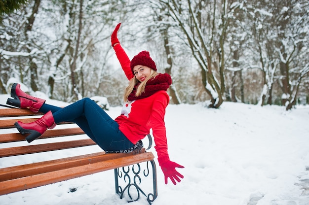 Rapariga loira com lenço vermelho, chapéu e camisola de papai noel posando no parque num dia de inverno.