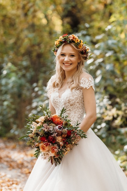 Rapariga loira com um vestido de noiva na floresta de outono