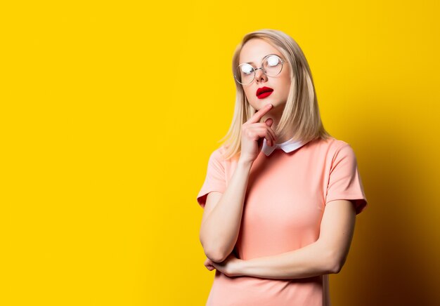 Rapariga loira com vestido rosa e óculos em fundo amarelo