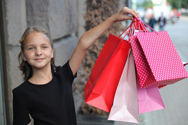 Rapariga loira de vestido preto com bolsas coloridas na mão estendida