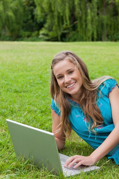 Rapariga olhando a câmera enquanto usa seu laptop e sorrindo