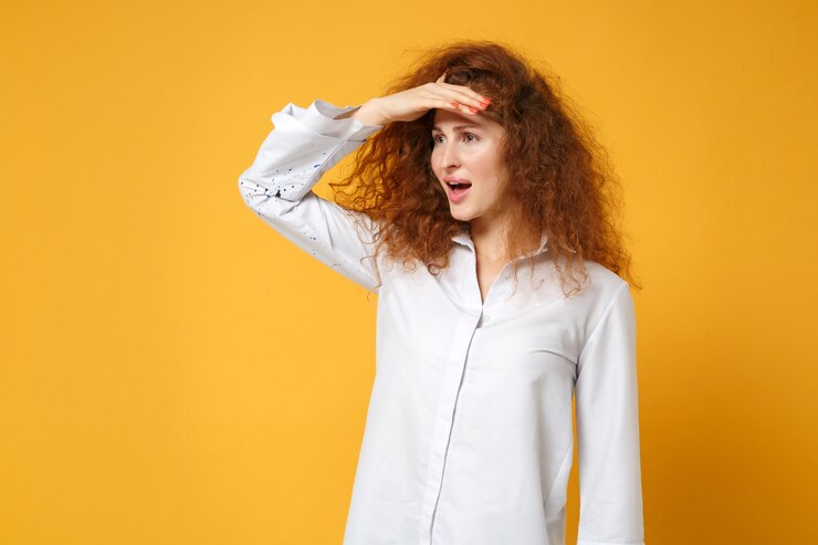 Foto rapariga ruiva com uma camisa branca casual posando isolada em uma parede amarelo-laranja