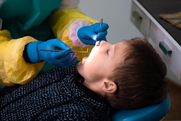 Rapaz 7-11 na cadeira do dentista e as mãos do médico com luvas azuis durante o exame ou tratamento dentário