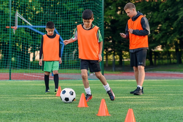 Rapaz adolescente aprende a circular a bola entre os cones de treinamento no estádio de futebol.