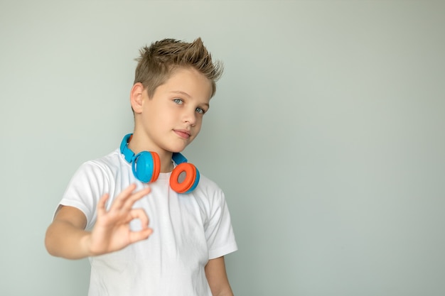 Rapaz adolescente com uma camiseta, mostrando o sinal de ok, com fones de ouvido sem fio no pescoço