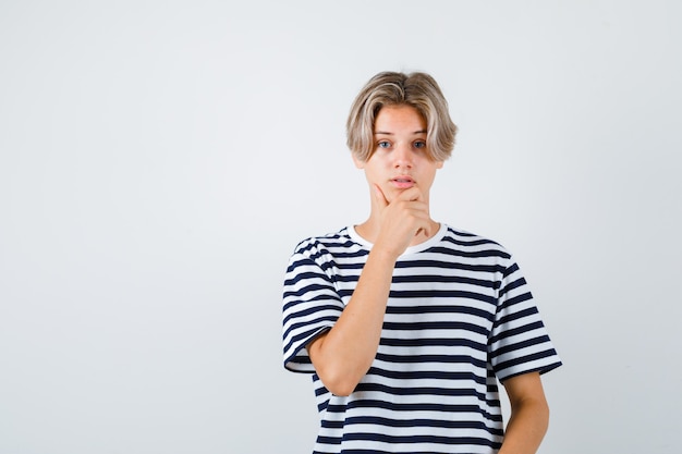 Rapaz adolescente, mantendo a mão no queixo em t-shirt e parecendo preocupado, vista frontal.