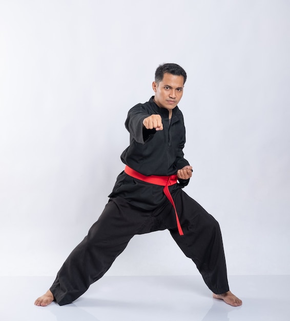 Rapaz asiático com um movimento de rebatida para a frente, vestindo um uniforme branco pencak silat