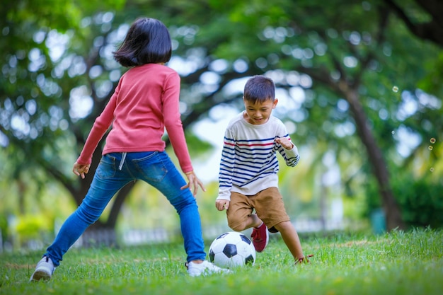 Rapaz asiático e menina desfrutando com jogo de futebol no exterior