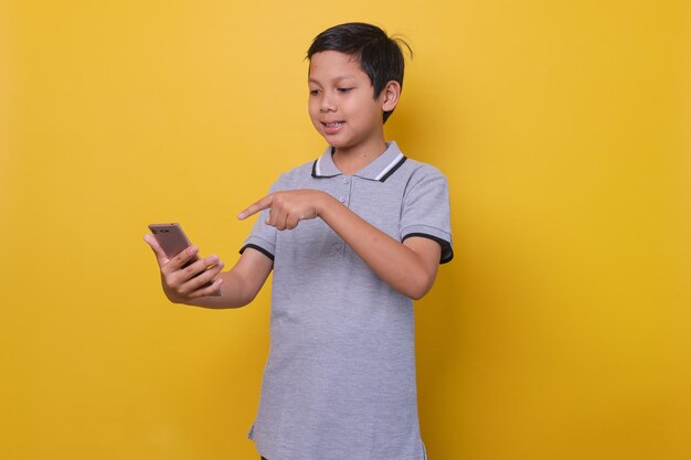 Foto rapaz asiático em estilo casual está sorrindo enquanto segura smartphone isolado em fundo amarelo online