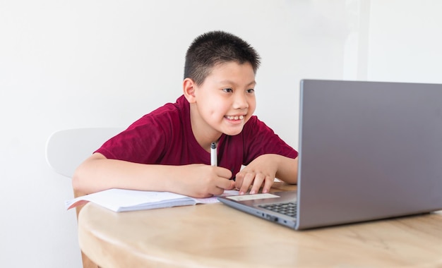 Rapaz asiático estudando online no laptop do computador com rosto sorridente e feliz em casa