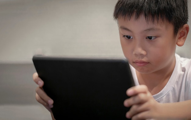 Rapaz asiático que joga o jogo no tablet digital em casa, crianças assistindo desenhos animados em taplet digital ou smartphone