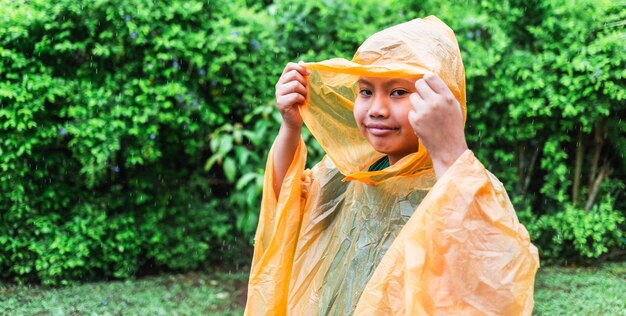 Rapaz asiático vestindo capa de chuva laranja está feliz e se divertindo na chuva em um dia chuvoso