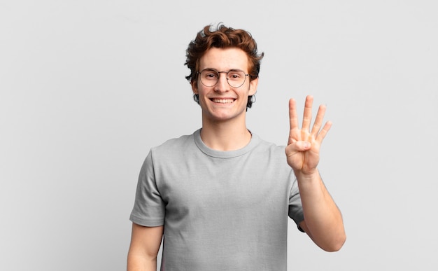 Rapaz bonito sorrindo e parecendo amigável, mostrando o número quatro ou o quarto com a mão para a frente, em contagem regressiva