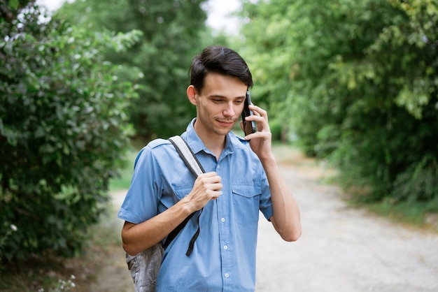 Rapaz de camisa azul com uma mochila na rua em um telefonema natural