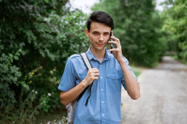 Rapaz de camisa azul com uma mochila na rua em um telefonema natural