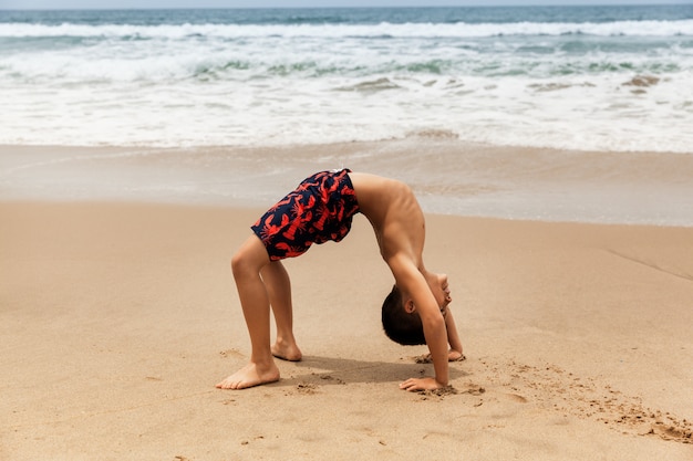 Foto rapaz desportivo praticando ioga na praia, férias de verão ativo na califórnia