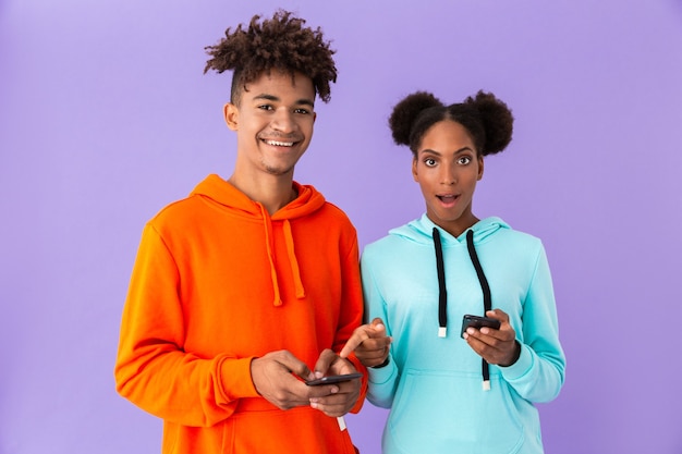 rapaz e rapariga usando smartphones, isolados sobre a parede violeta