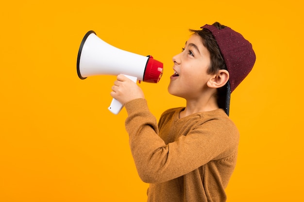 Rapaz europeu atraente gritando notícias em um megafone para um cartaz em um fundo laranja do estúdio.