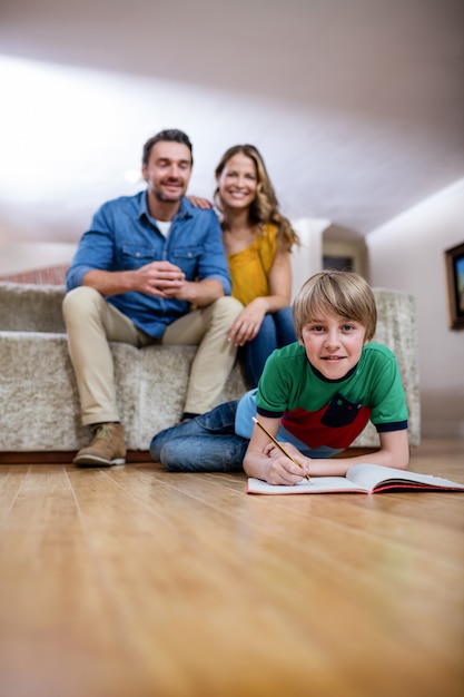 Rapaz fazendo lição de casa enquanto os pais sentados no sofá