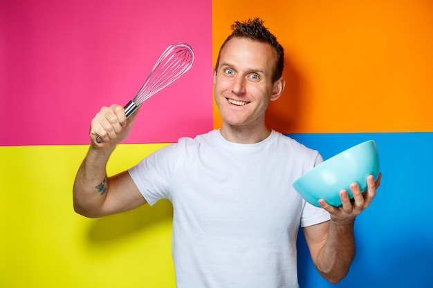 Rapaz jovem com uma camiseta branca, fundo colorido, utensílios de cozinha, cozinheiro, foto de emoções