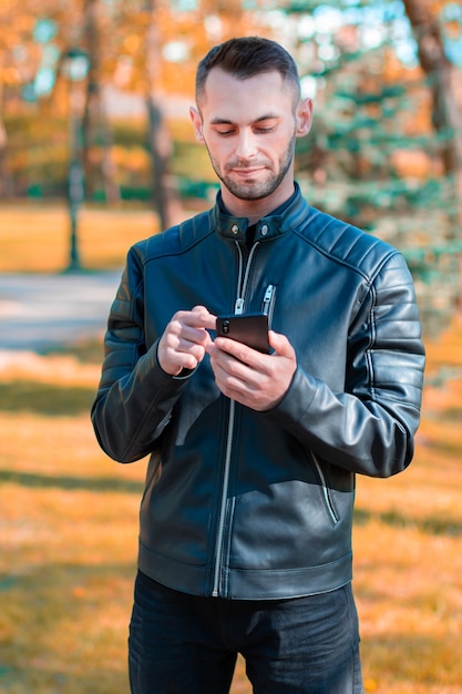 Rapaz jovem usando smartphone preto no belo parque de outono