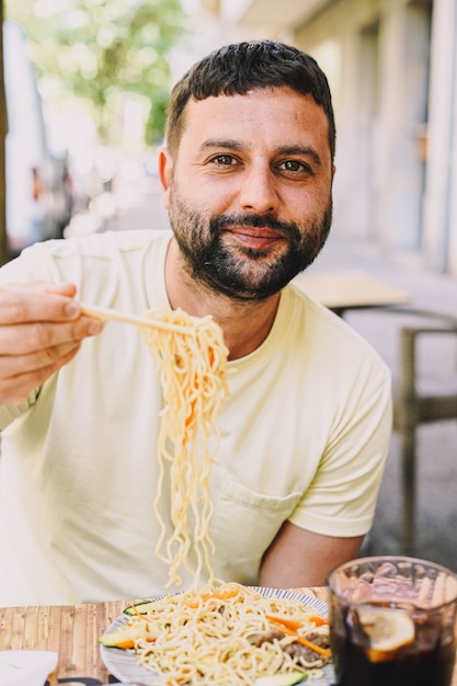 Rapaz latino de t-shirt amarela a comer comida japonesa