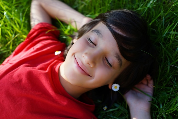 Rapaz pequeno desfrutando de um horário de verão deitado no prado grama verde com raio de sol no cabelo