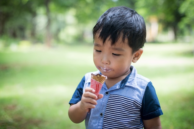 Rapaz pequeno que come o gelado no campo de jogos com tempo feliz.
