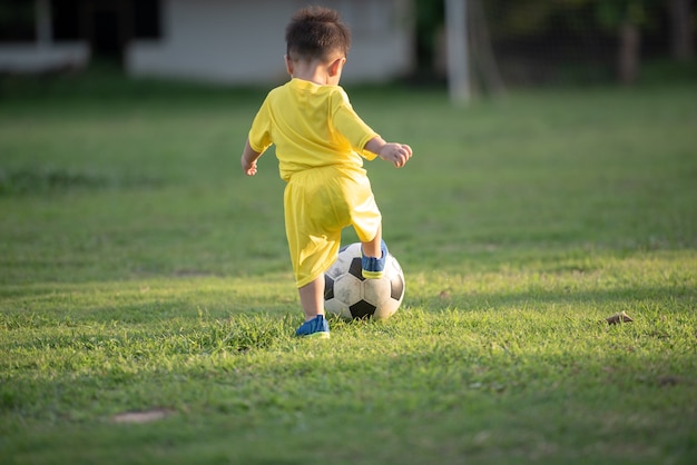 Rapaz pequeno que joga o futebol no campo.