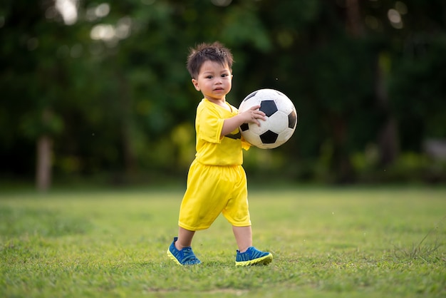 Rapaz pequeno que joga o futebol no campo.