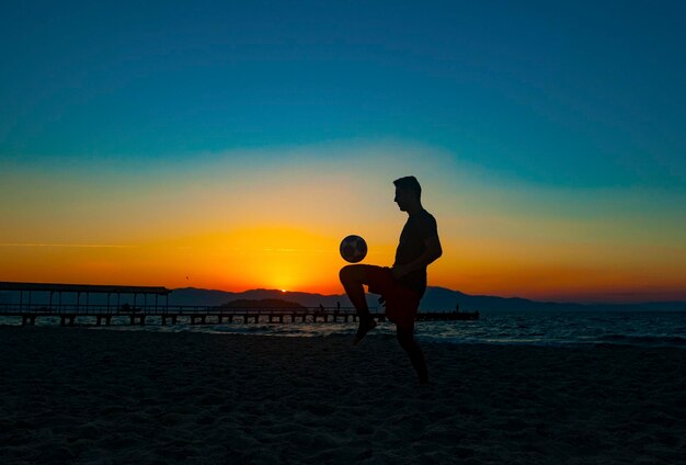 Rapaz praticando esportes com bola na praia em pleno pôr do sol de verão na costa brasileira