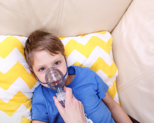 Rapaz respirar através do nebulizador. Criança doente com nebulizador pediátrico.