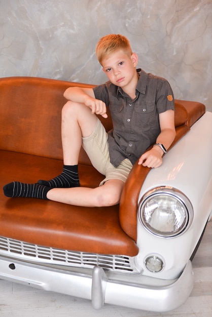 Foto rapaz sentado no interior do estúdio em uma cadeira sob a forma de um carro retrô. móveis vintage criativo