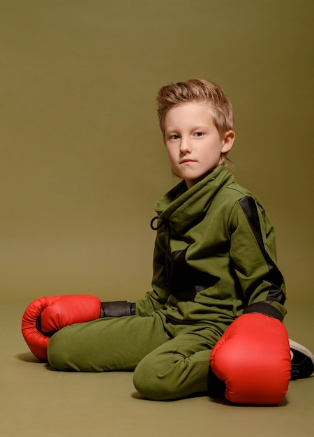 Rapaz sério no verde em luvas de boxe vermelhas, garoto cansado