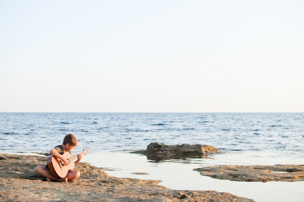 Foto rapaz tocando violão pelo oceano.