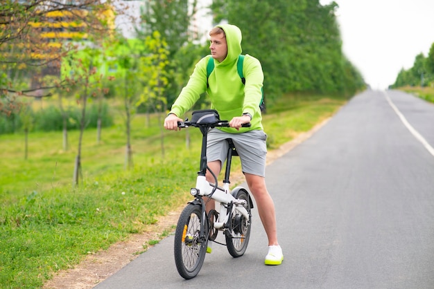 Rapaz triste andando de bicicleta elétrica em um parque de verão.