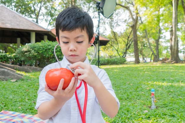 Rapaz usar estetoscópios e brincar com o símbolo de tomate de fruta