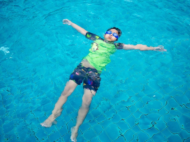 Rapaz vestindo um maiô e óculos nadando no meio da piscina com fundo de água azul