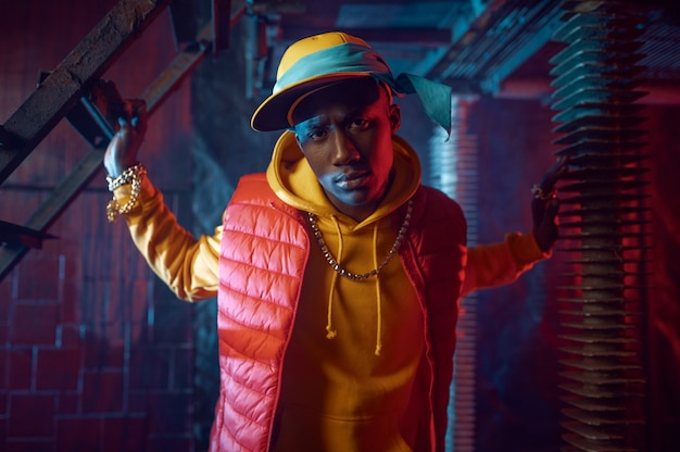 Rapper elegante com capuz amarelo posando com uma decoração subterrânea legal. Artista de hip-hop, cantora de rap, performance de break