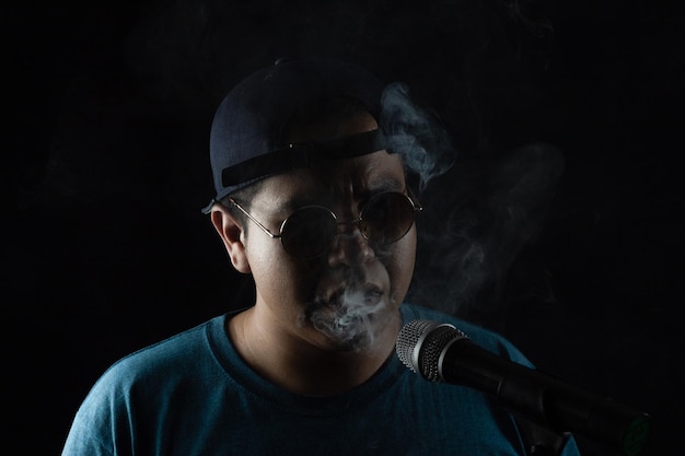 Rapper latino fumando e soprando fumaça perto do microfone, iluminado pelas luzes do palco.