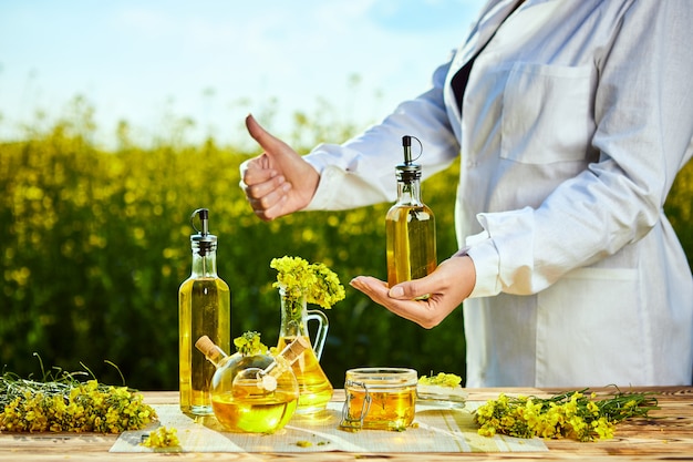 Rapsölflasche in der Hand eines Agronomen oder Biologen auf Hintergrundvergewaltigungsfeld